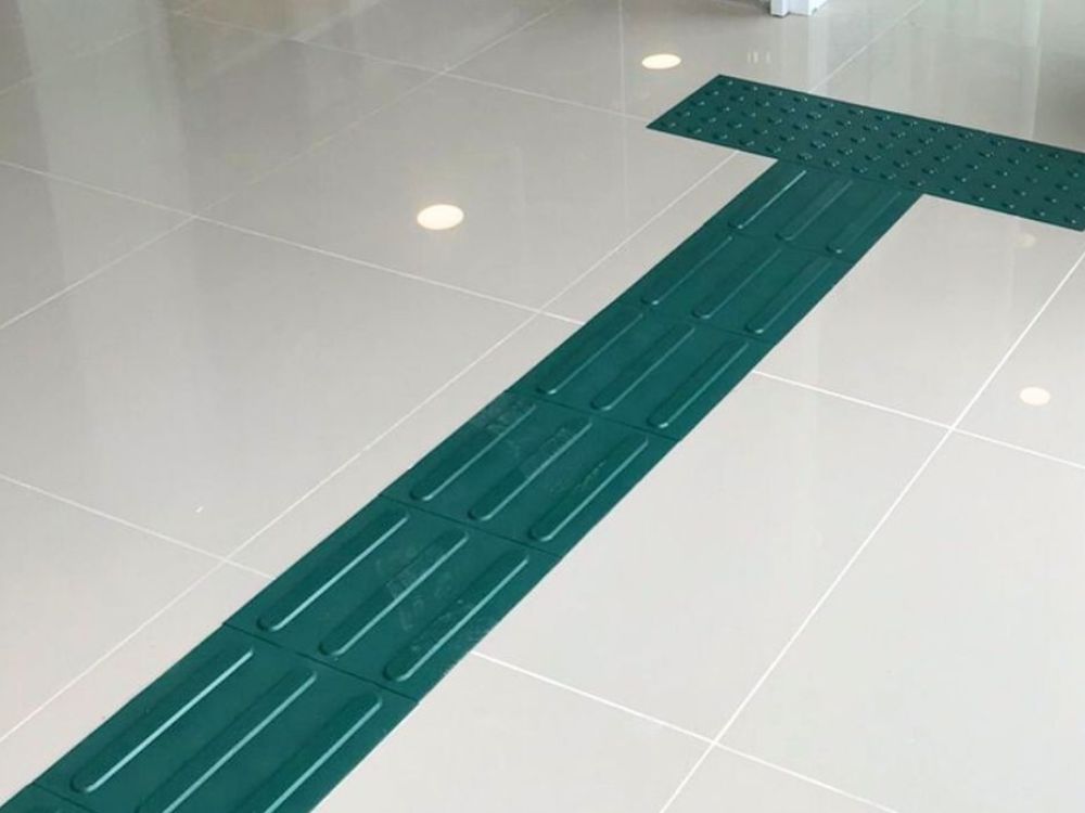 Piso tátil direcional instalado em área interna, mostrando claramente o que é piso tátil e como ele orienta o caminho.