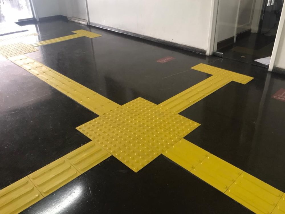 Instalação de piso tátil amarelo em cruzamento de corredores, representando o que é piso tátil em sinalização acessível.