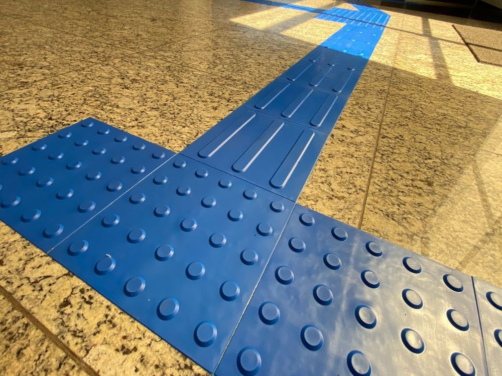 Piso tátil nas cores azul e cinza instalado em ambiente corporativo, exemplificando na prática o que é piso tátil e sua aplicação.