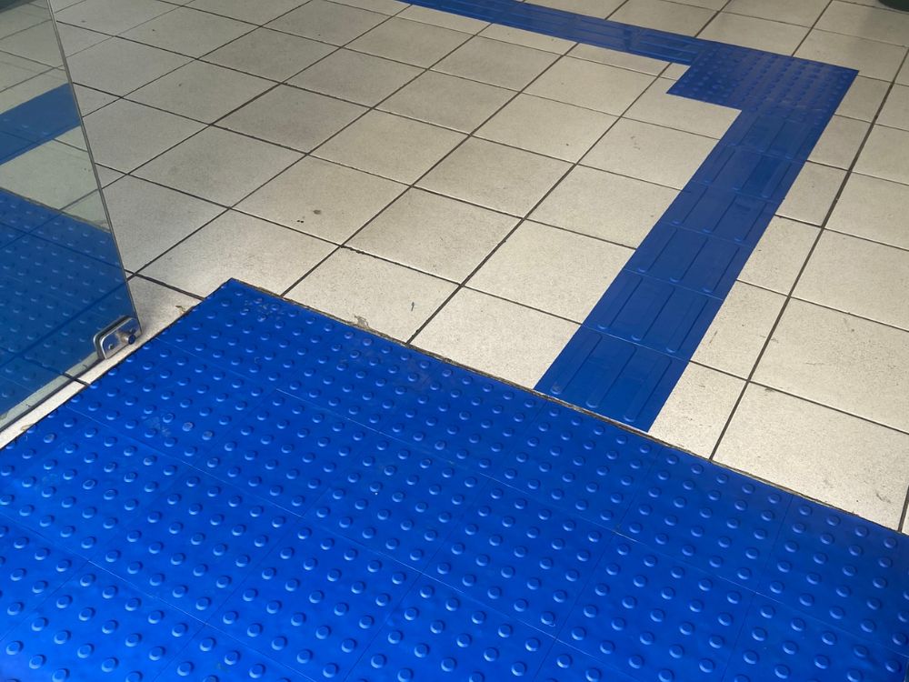 Interseção com piso tátil direcional e de alerta azul, exemplo dos diferentes tipos de piso tátil em ambientes comerciais.