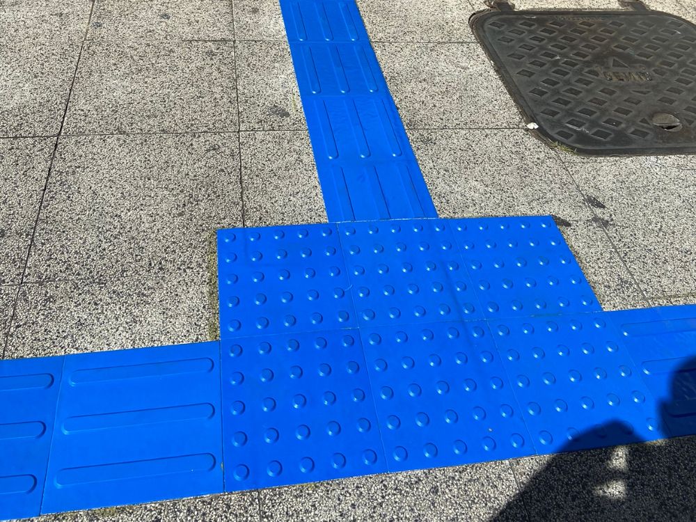Calçada acessível com piso tátil azul direcional e de alerta instalado em área urbana, garantindo orientação e segurança a pessoas cegas.