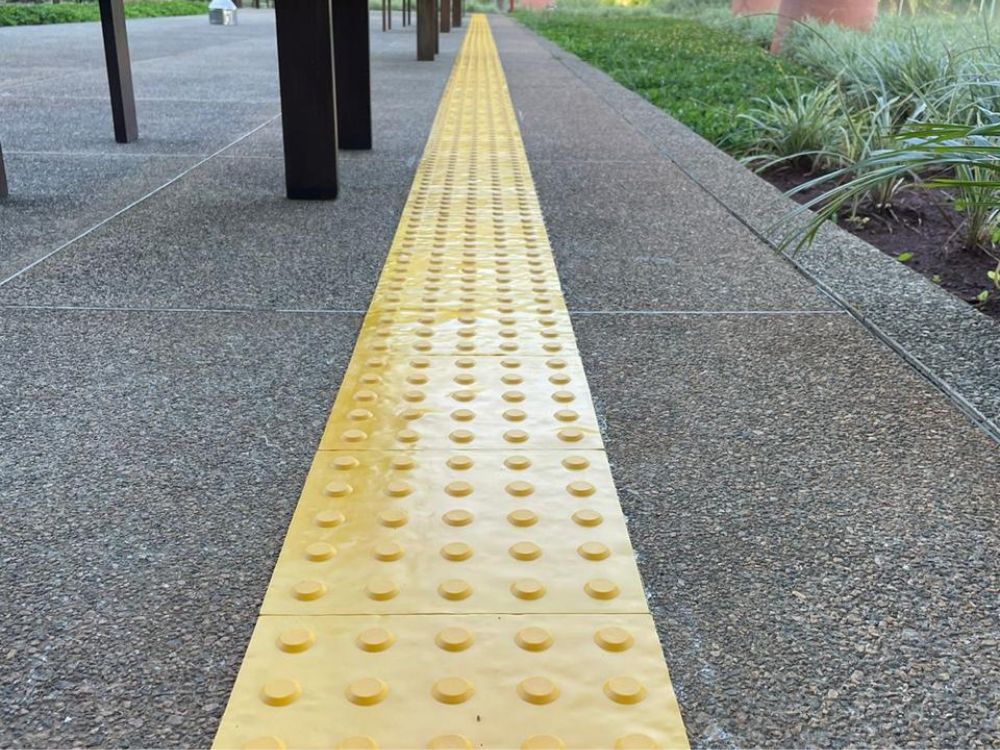 Calçada acessível com piso tátil amarelo de alerta instalado em área externa, garantindo orientação e segurança para pessoas com deficiência visual.