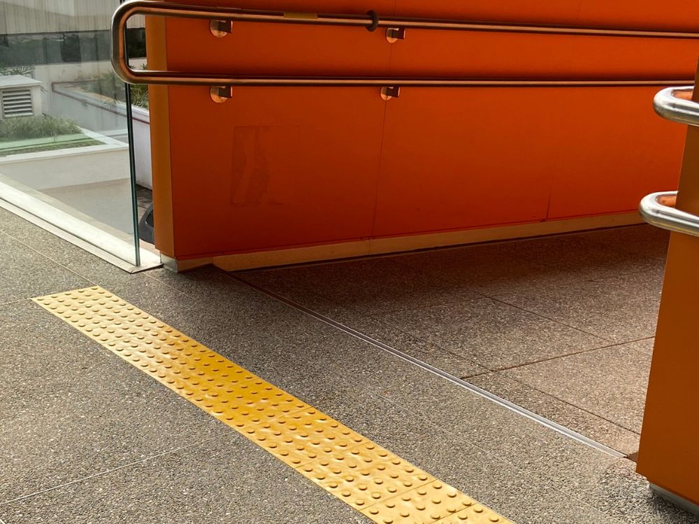 Piso tátil em rampa instalado próximo a corrimão, com sinalização de alerta para indicar início e fim do percurso acessível