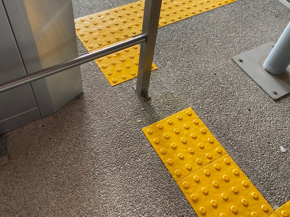 Piso tátil em rampa com sinalização amarela de alerta indicando mudança de nível e auxiliando na orientação segura de pessoas com deficiência visual