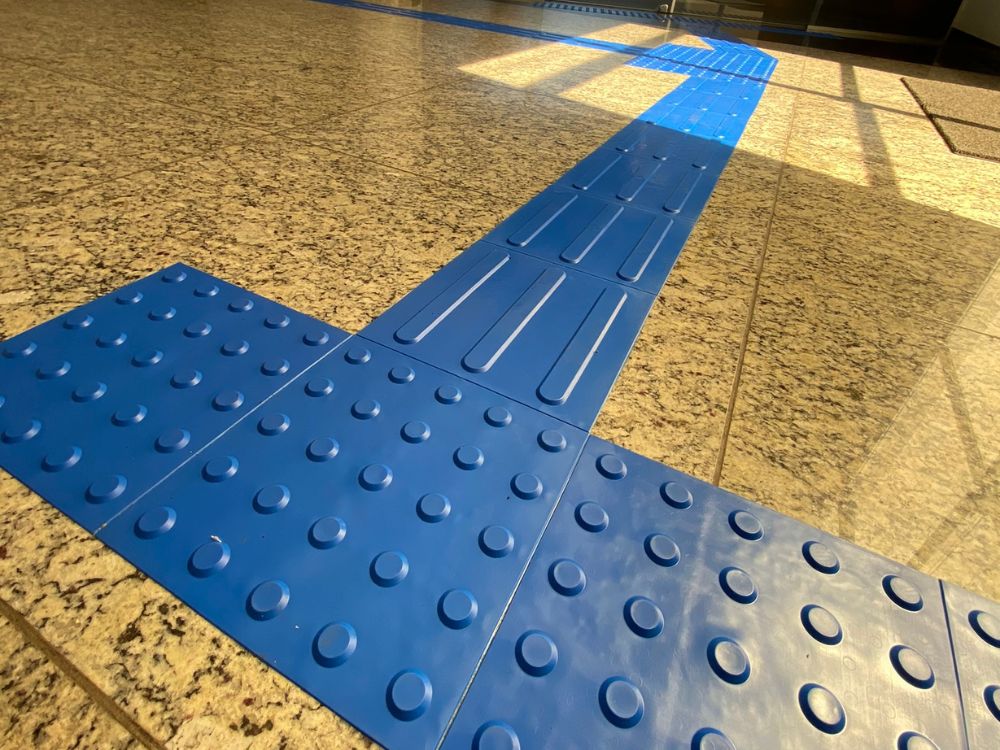 Piso direcional azul instalado em ambiente interno, demonstrando o tamanho do piso tatil e sua aplicação para acessibilidade em circulação.