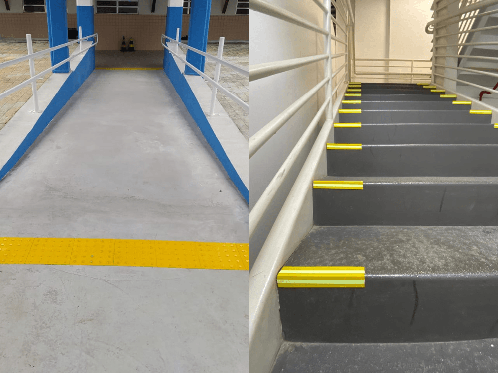 Rampa com corrimãos laterais e piso tátil amarelo aparece ao lado de uma escada com faixas contrastantes nos degraus.